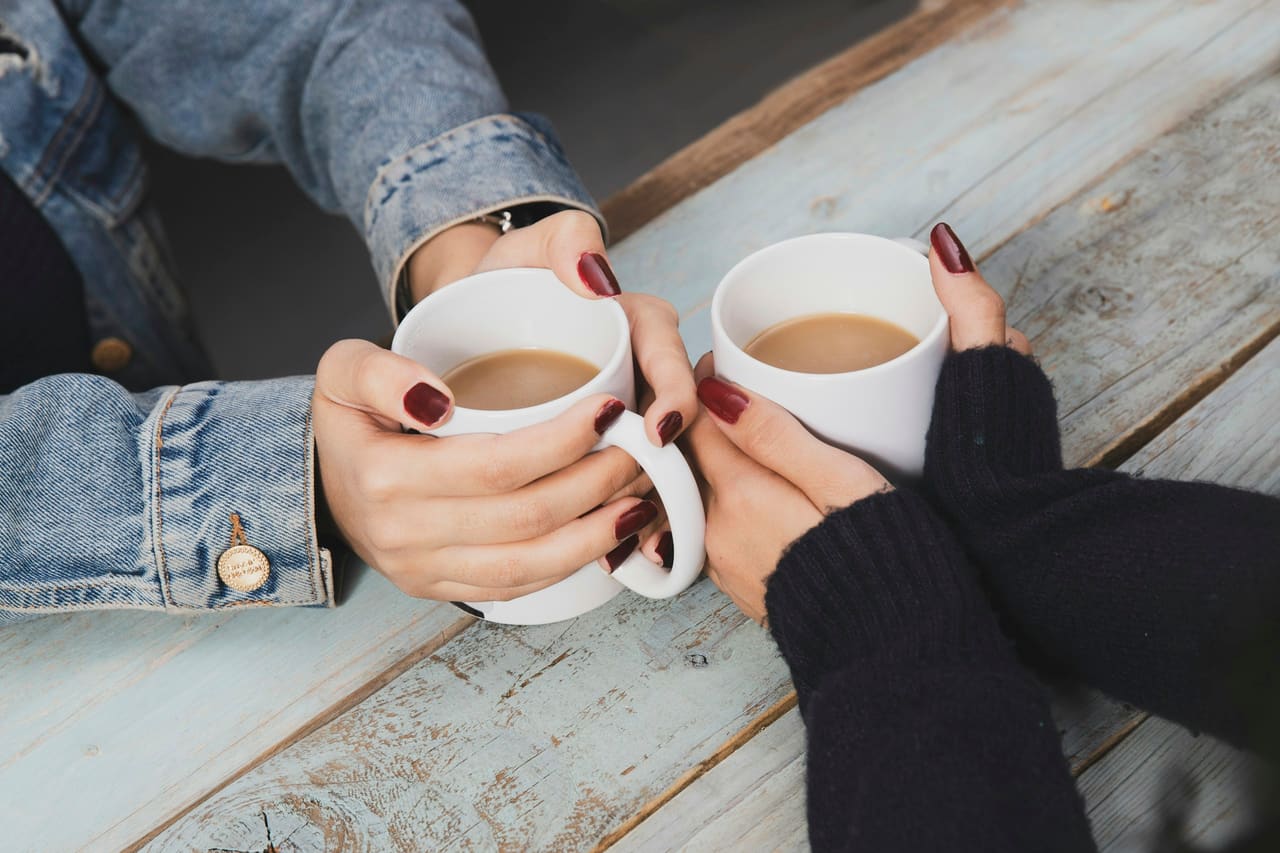 Two people's hands holding mugs across a wooden table